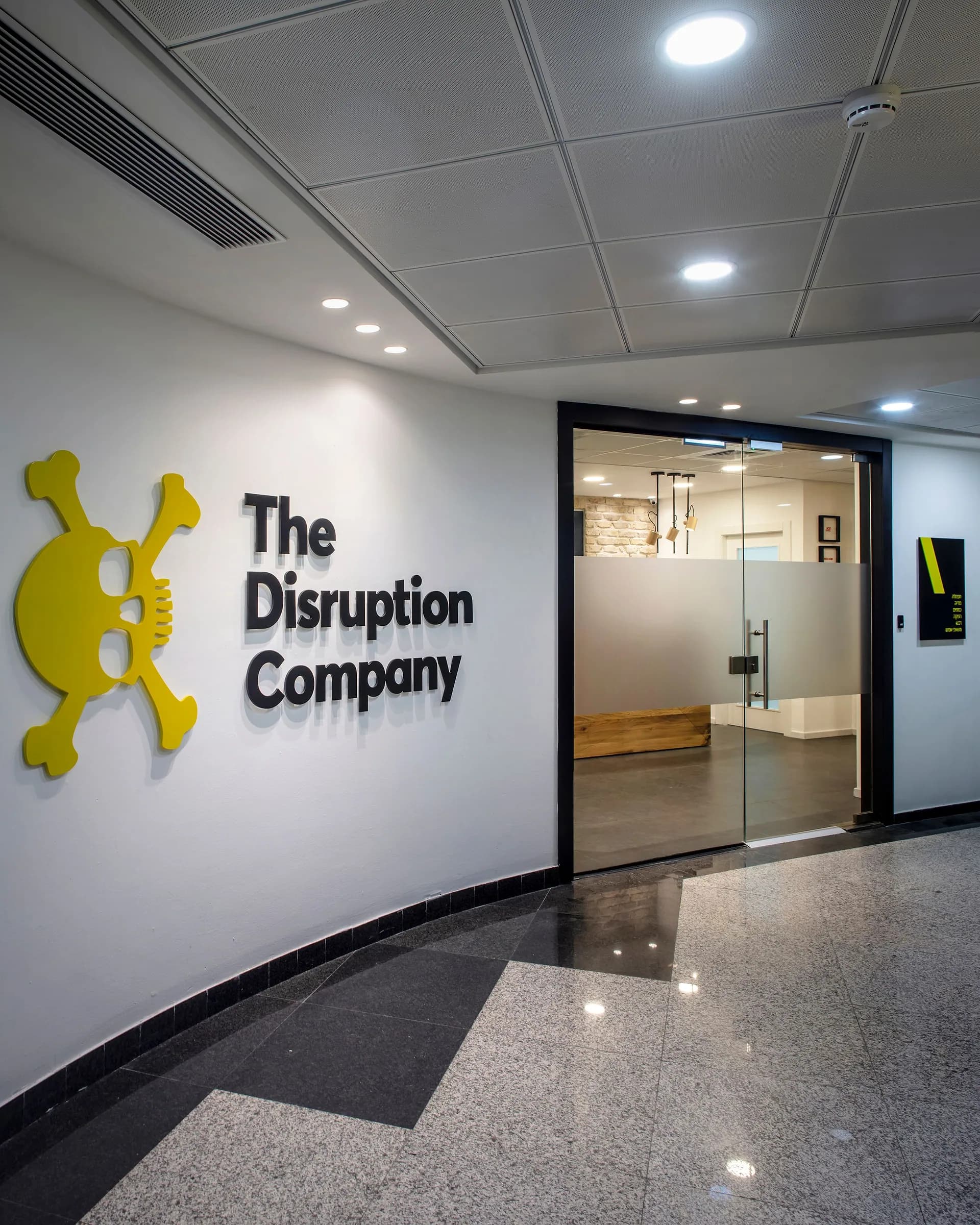 כניסה למשרד עם קיר זכוכית ולוגו The Disruption Company על הקיר
