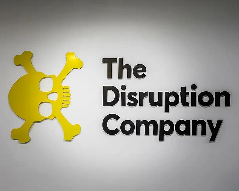 קיר לבן עם לוגו The Disruption Company ואלמנט גרפי צהוב