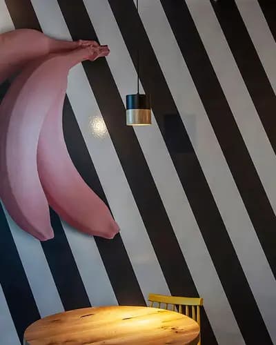 קיר פסים שחור לבן עם אלמנט בננות ורודות ושולחן עץ בחזית